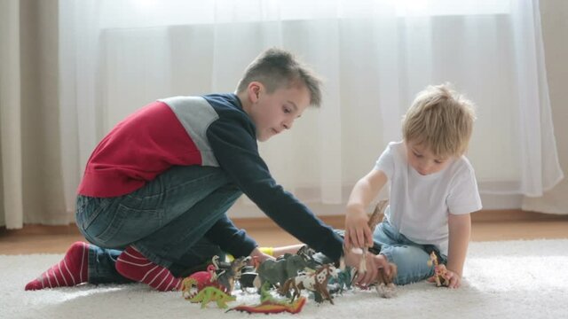 Blond child, toddler boy and his older brother, preteeen boy, playing with plastic animal toys at home, soft back light