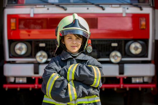 Child, cute boy, dressed in fire fighers cloths in a fire station with fire truck