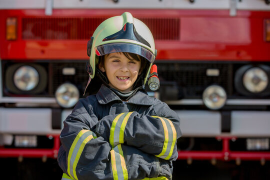 Child, cute boy, dressed in fire fighers cloths in a fire station with fire truck
