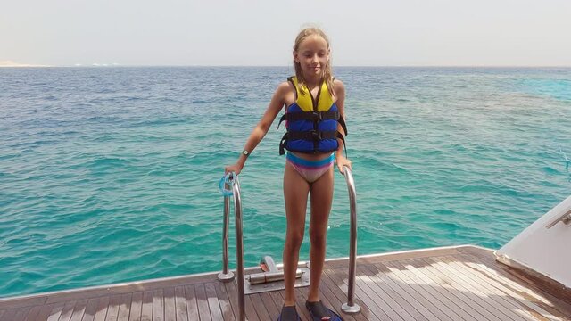 Smiling girl in swimwear and flippers standing near sea. Cute happy teenage girl in life jacket and flippers standing on wooden surface after swimming in sea