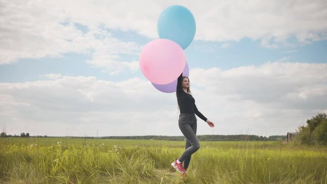 Happy girl with big multicolored balloons posing on the field.