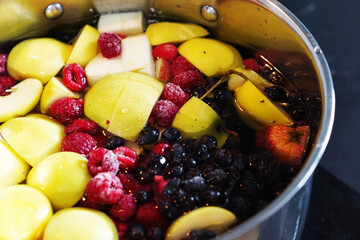 We are preparing a delicious compote from apples, cherries, raspberries, irgi. Fresh fruits and berries are boiled in a metal pan on the stove.