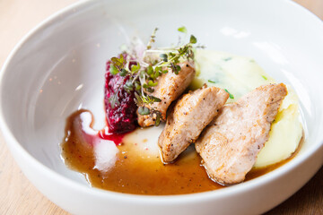Delicious roasted pork filet cooked with smashed potatoes and smashed beetroots served in white plate.
