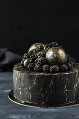 Black cake on a dark background. A cake for Halloween. A pie decorated with blackberries and golden balls. Festive dessert with berries. Happy Halloween