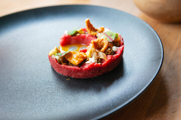 Fresh traditional polish beef tartar served with mushrooms, mustard and fresh lettuce on black ceramic plate ready to be served