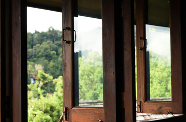 Dark brown wooden window open and outside is blurry scenery of green mountain.