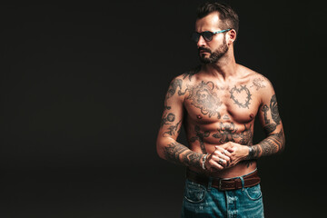 Fototapeta premium Portrait of handsome confident stylish hipster lambersexual model. Sexy modern man. Naked torso with tattoos.Fashion male posing in studio on dark background. In sunglasses