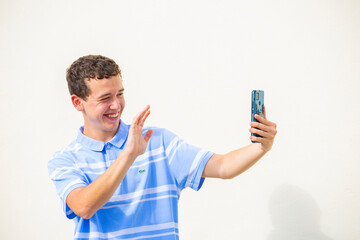 chico joven sonriente saludando con la mano en una videollamada con telefono movil con camiseta...