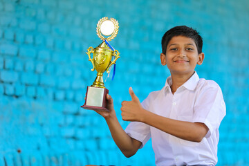 Clever schoolboy raising his trophy as a winner in school competition.