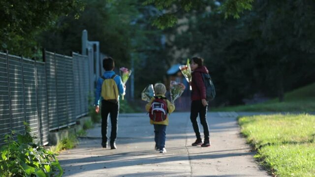 Happy children, going to school in the morning, first day, caring bouquet of flowers for the teacher, walking together
