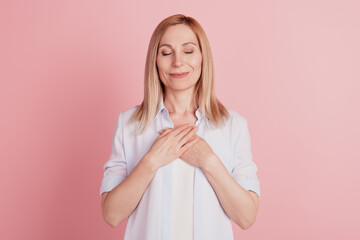Portrairt of lovely young woman close eyes hands palms on chest grateful isolated over pink...
