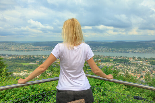 backside of woman looking Zurich city lake and skyline from top of Felsenegg cable car. Blonde tourist woman by lakefront in Deutch Switzerland of Canton of Zurich.