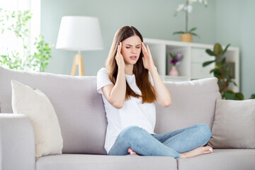 Portrait of attractive frustrated sick girl touching temple feeling bad sitting on divan staying...