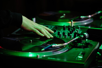 Hand of hip hop dj scratching vinyl record on turntables in green neon lights on concert stage....