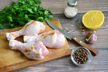 cooking chicken legs with lemon, pink salt, garlic, allspice and parsley on cutting board on...