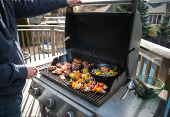 Man grilling chicken and vegetables outdoors on a gas bbq grill.