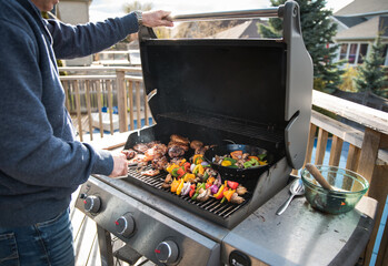 Man grilling chicken and vegetables outdoors on a gas bbq grill.