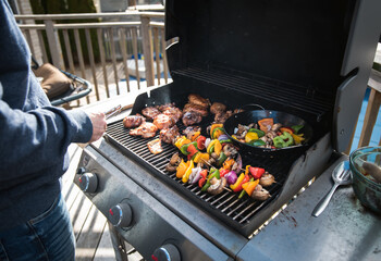 Man grilling chicken and vegetables outdoors on a gas bbq grill.