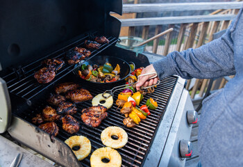 Man grilling chicken, vegetables and pineapple on a gas bbq grill.