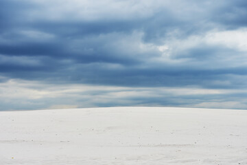 Landscape with dark blue clouds over light sand dunes.