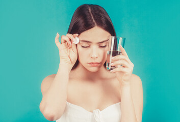 Woman taking drugs to releave headache. Brunette take some pills, holds glass of water, isolated on...