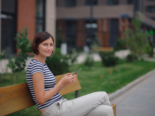 Smiling asian woman using mobile phone in the city street. checking mobile phone. student woman looking at the screen. lady e-learning via her gadget