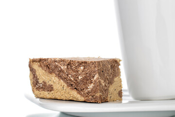 Pieces of sweet halva with chocolate on a white saucer with a white cup, close-up, isolated on white.