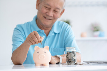 Elder man smiling putting a coin inside piggy bank.