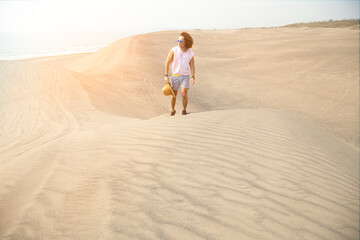 Fototapeta na wymiar Young male with curly hair, walking on sand dunes during golden hour