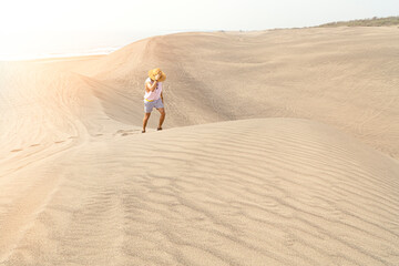 Young male holding his hat, walking on sand dunes during golden hour