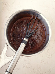 Black whisk in metal pot chocolate dough cake making flat lay