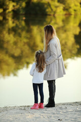 Mother and daughter walk on beach near river.