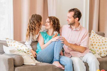 Happy family, mom dad and daughter are sitting on couch and laughing together