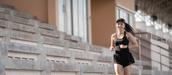 Obraz premium A healthy adult Asian woman running up on concrete stairs of the city stadium to strengthen body