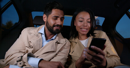 Diverse couple riding in cab and surfing internet on smartphone