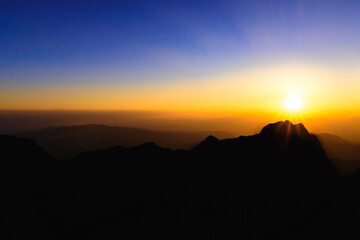 A stunning sunset or sunrise scene of silhouette mountain peaks and purple ridges with the twilight background, the blue sky and the pink-yellow skyline, captured at chiangmai, thailand