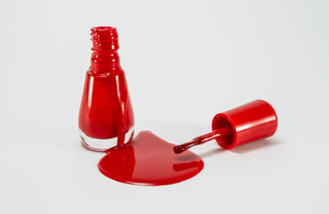 Red nail polish spilled from a glass bottle on a white background.