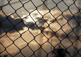 Fototapeta premium Steel mesh fence with blurred sunset background.