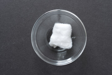 cotton ball in a clear glass bowl on a dark gray paper background