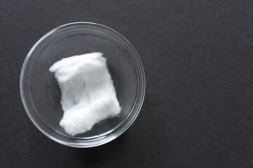 cotton ball in a clear glass bowl on a dark gray paper background