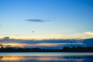 Silhouette paramotor pilots flying over a lake with the sunset sky background