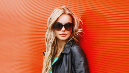 Stylish portrait of beautiful blonde woman wearing a black rock jacket and sunglasses on red...