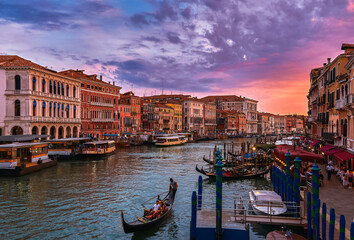 Fototapeta na wymiar Sunset view of Grand Canal, Venice, Italy. Vaporetto or waterbus station, boats, gondolas moored by walkways, beautiful sunset clouds, UNESCO heritage