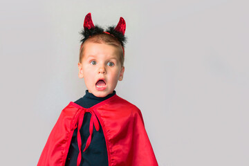 Frightened little toddler boy in a carnival costume for Halloween is isolated on a grey background. Traditions, holidays concept.