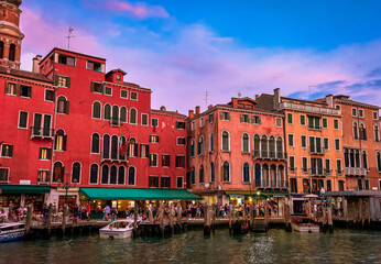 Sunset view of waterfront buildings of Venice, Italy. Boats moored by walkways, beautiful sunset clouds, UNESCO heritage, evening, tourists walking
