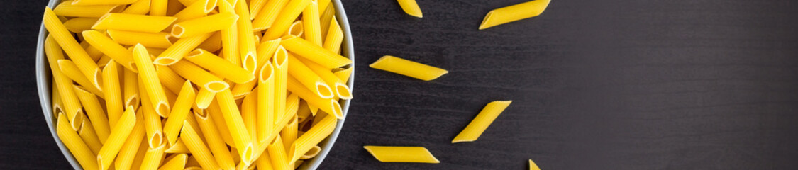 banner of Top view of black background with italian raw penne or pasta in bowl with copy space