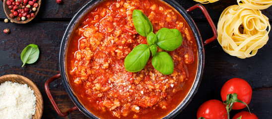 Traditional italian Bolognese sauce in saucepot an old dark wooden background. Top view, copy space