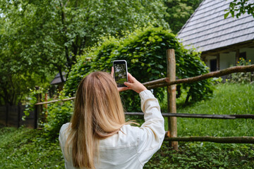 Naklejka premium Girl holds a mobile phone in her hands and takes pictures of nature in the park to share photos on social networks. Focus on the phone screen. Make memories using your smartphone. Mobile phone closeup