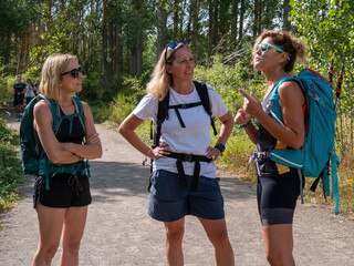 A group of blonde Caucasian backpacker girlfriends wearing sunglasses, wearing summer clothes on a hot day chatting on a trail in the countryside