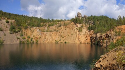 An abandoned stone quarry filled with water and trees around.